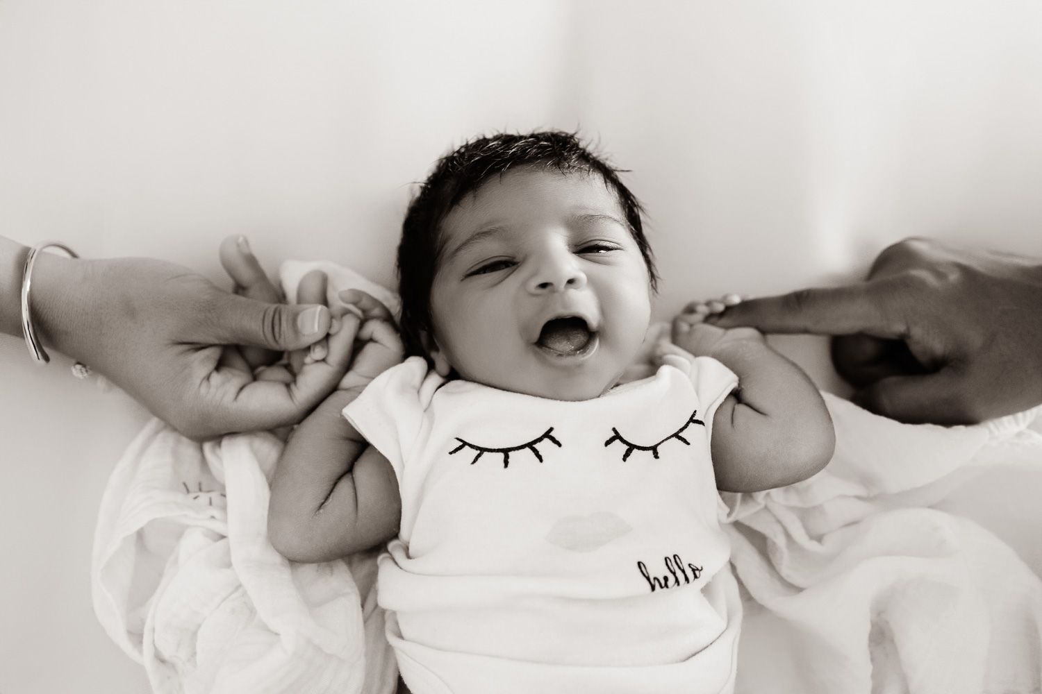 A newborn baby holds mom and dad's fingers while smiling into the camera during her newborn photography session in the Bay Area