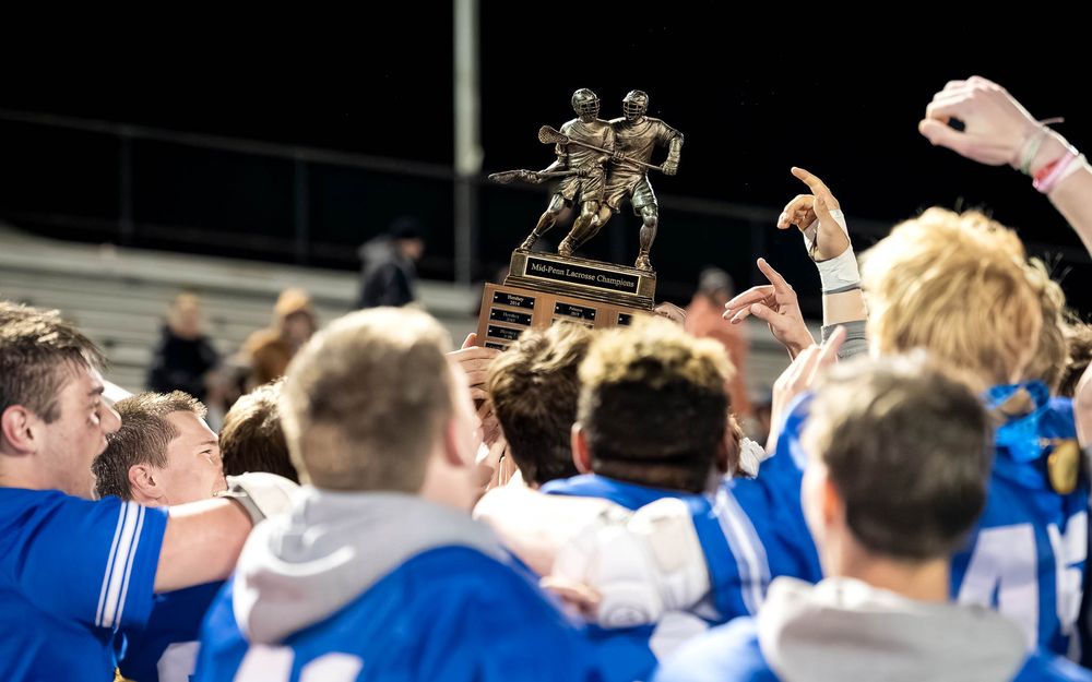 Lower Dauphin lacrosse players huddle around the championship trophy after the 2026 Mid Penn title win by SportsFox Photography, Hershey PA.