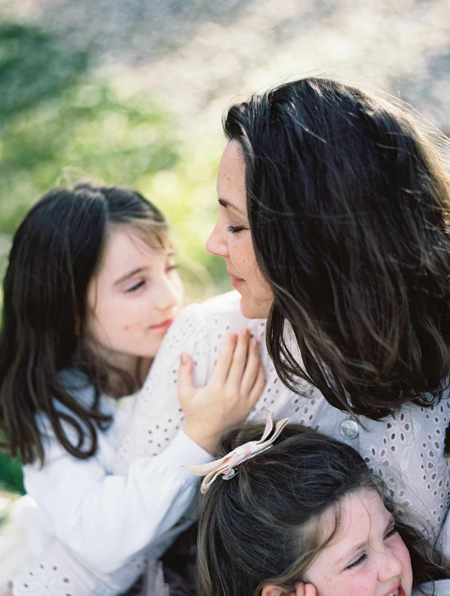 A mother gazes lovingly at her young daughter in a warm, intimate outdoor family portrait.