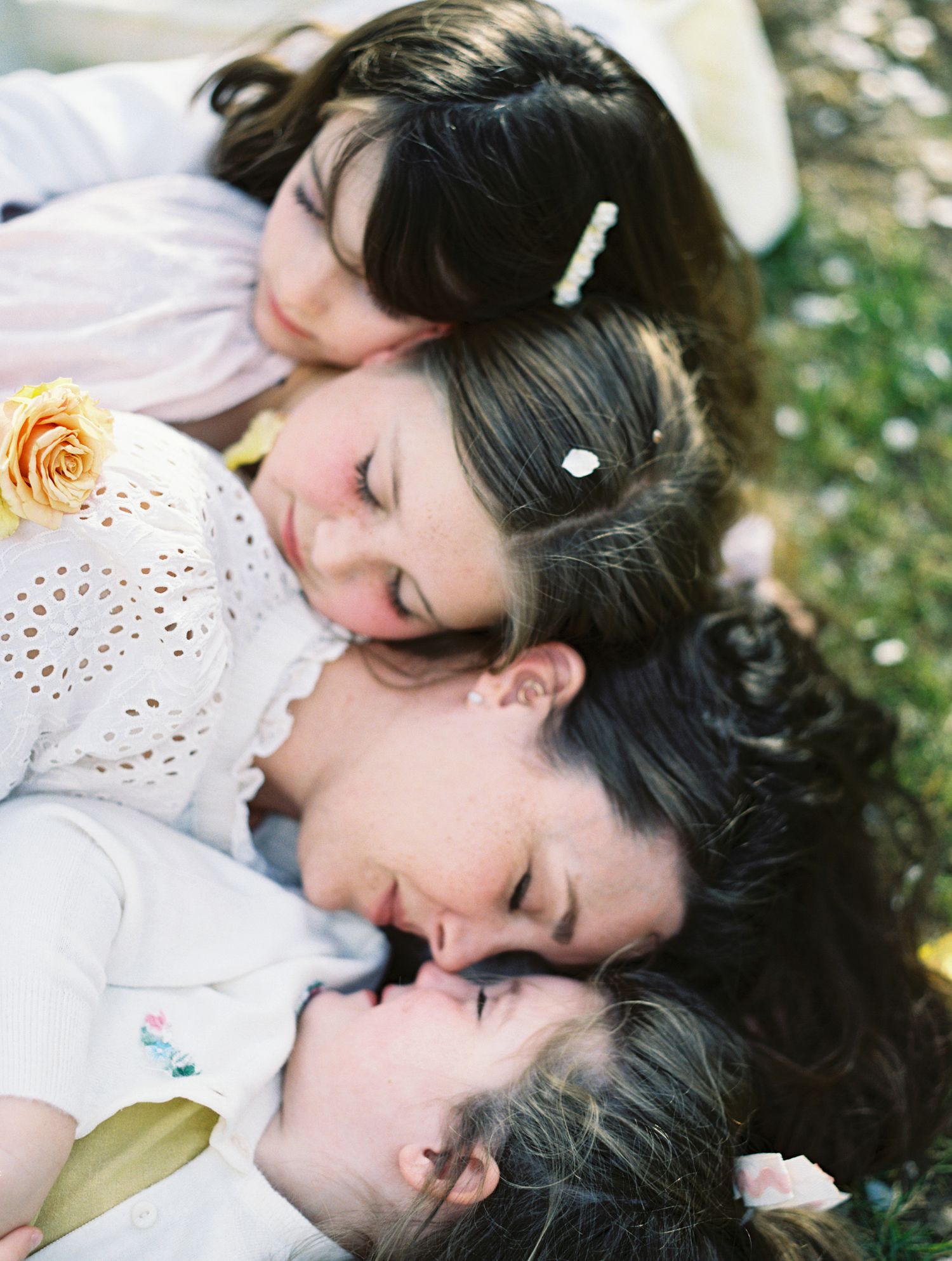 A tender moment as a mother and three daughters lie together in the grass with flowers.