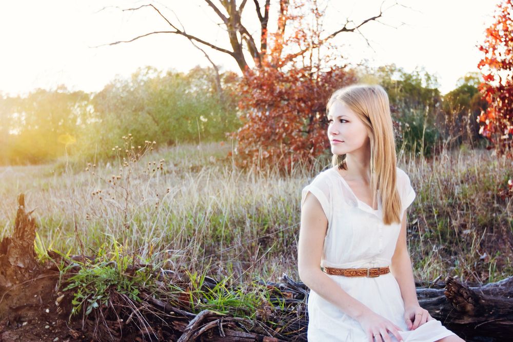 Senior portrait near Brighton Michigan; girl sitting on log in field with cinematic aesthetic by South Lyon, MI photographer
