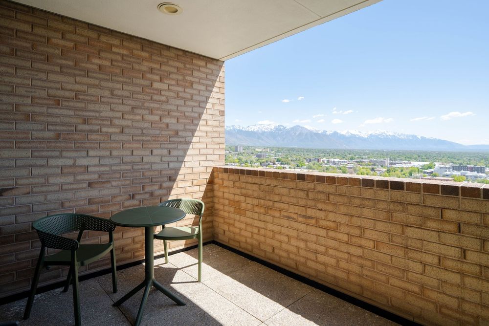 Elevated brick balcony with green table and chairs offering panoramic mountain and city views on a clear day.