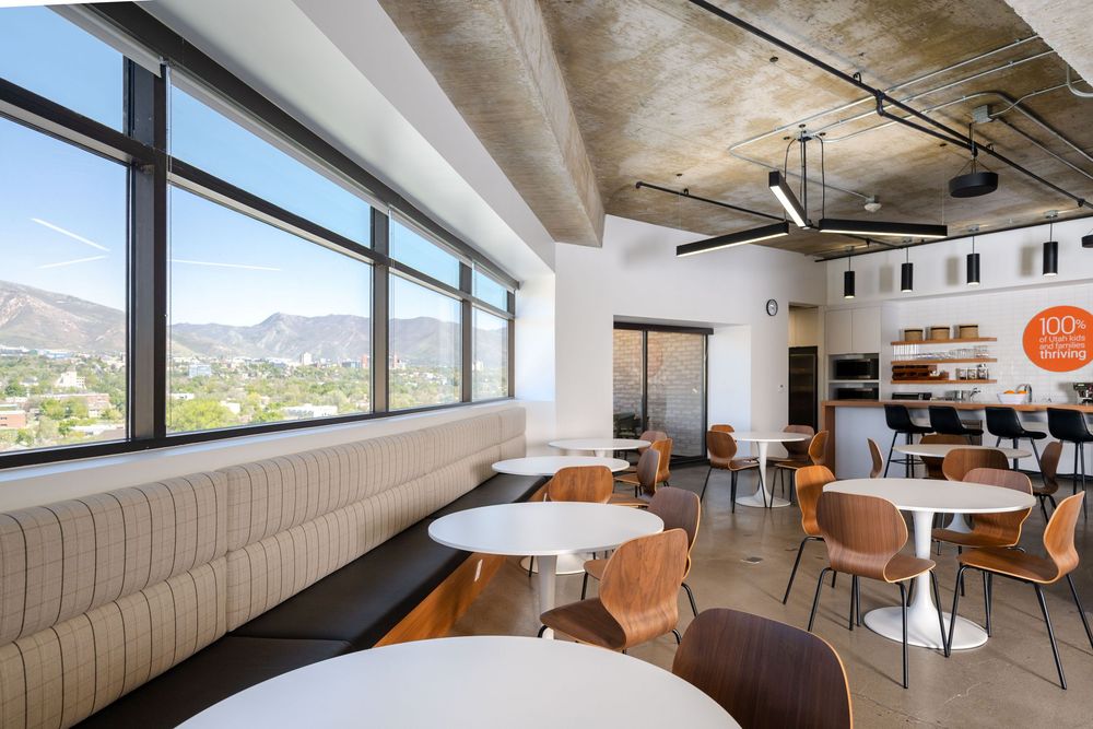 Bright modern cafe lounge with mountain views, booth seating, round tables, and exposed concrete ceiling design.