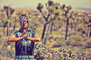 Man in colorful festival attire meditates with prayer hands in Joshua Tree desert.