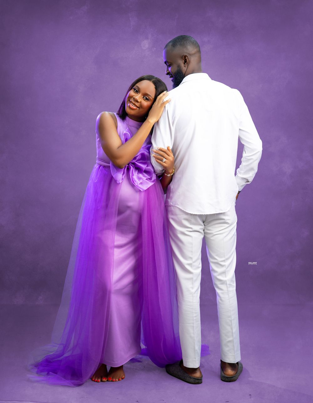A romantic pregnancy photo shoot with couple in purple dress and white suit against a dreamy purple background.