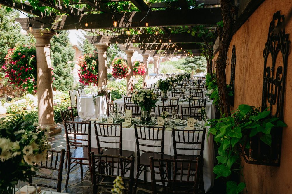 Elegant outdoor wedding reception under a pergola with chiavari chairs, white tablecloths, and lush garden surroundings.