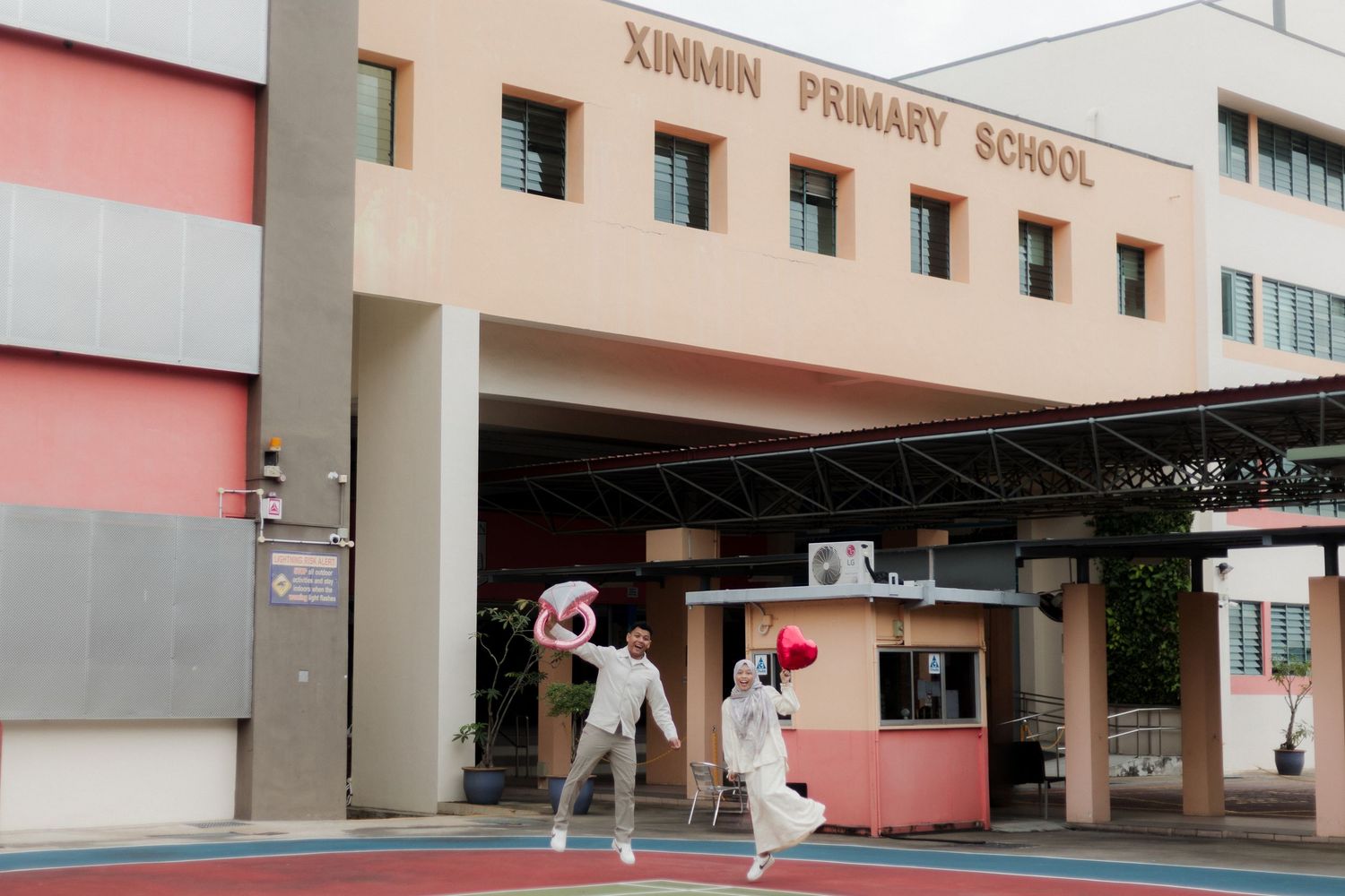 Two students play outside Xinmin Primary School, a pink building with a covered entrance in Singapore.