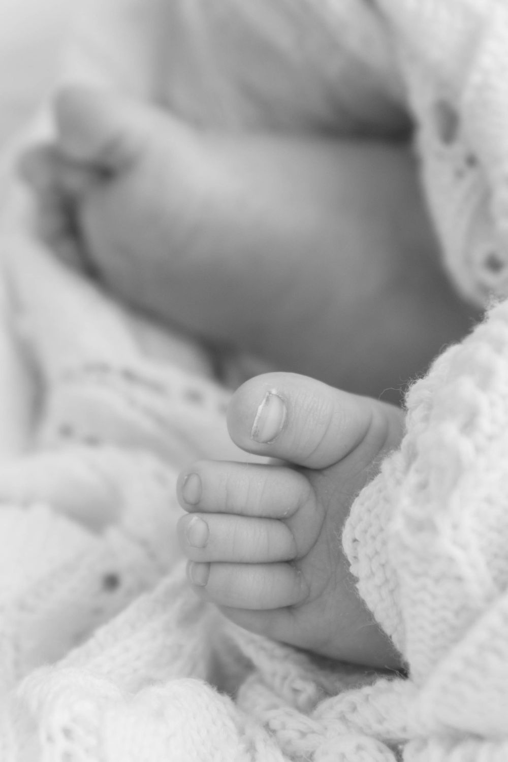 Close-up black and white photo of a newborn baby's tiny hand and fingers wrapped in a soft knit blanket.