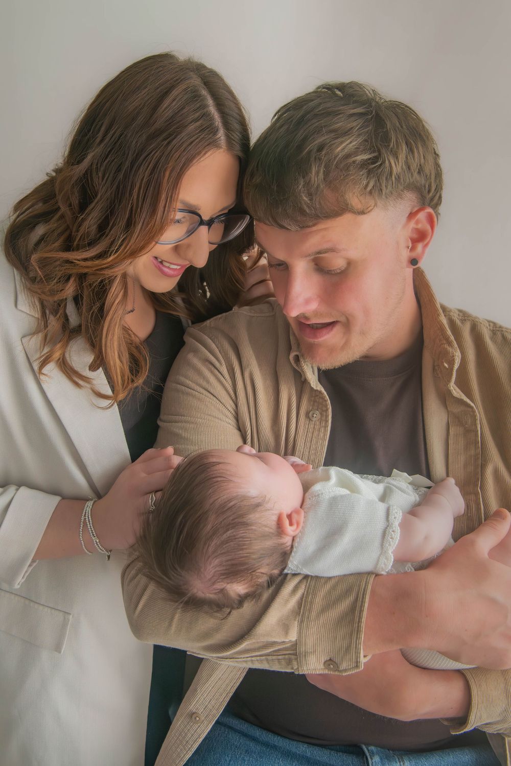 Young couple smiling and gazing lovingly at their newborn baby during a professional family portrait session.