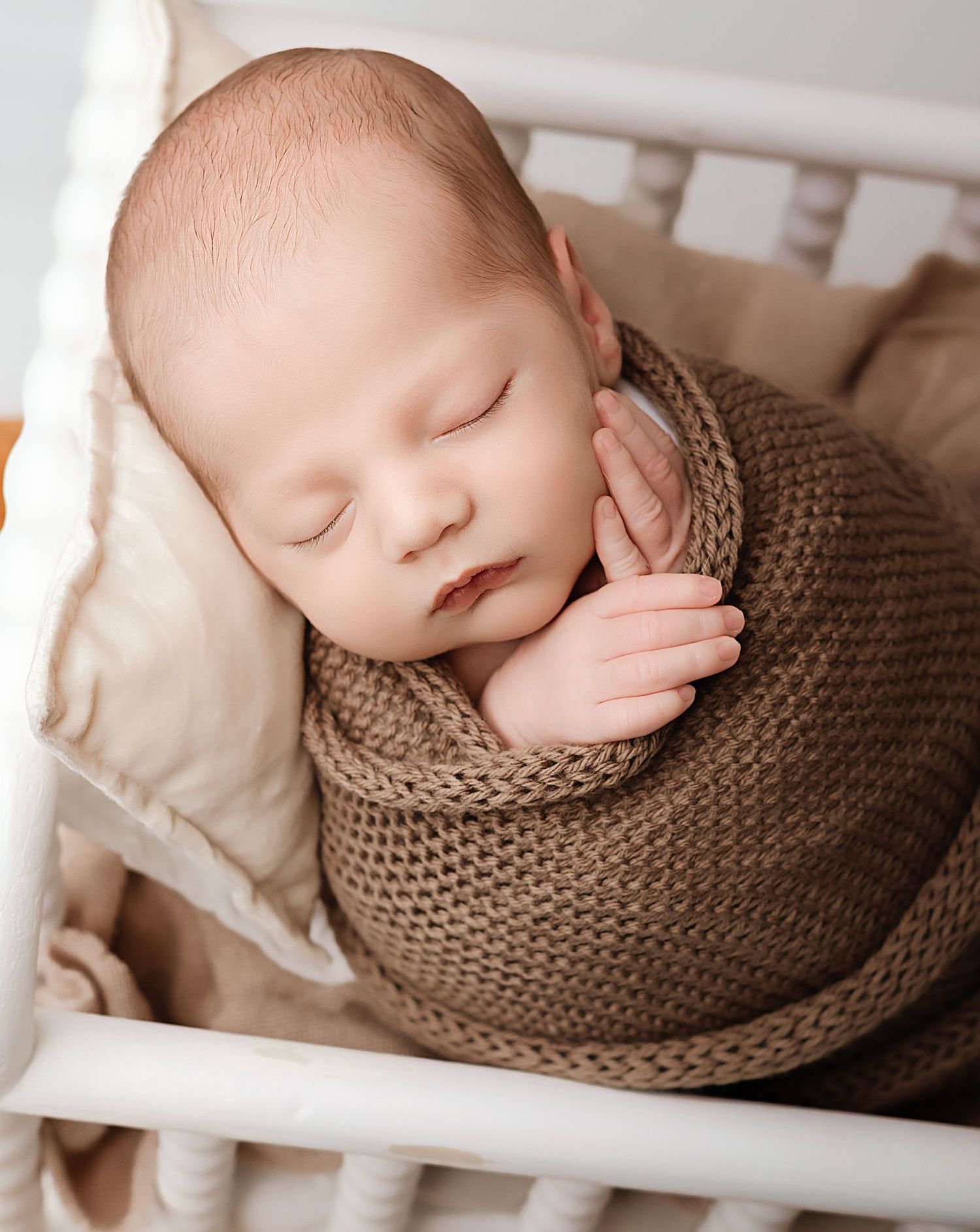 An alert newborn baby with wide eyes lies on a soft white blanket in a peaceful portrait.