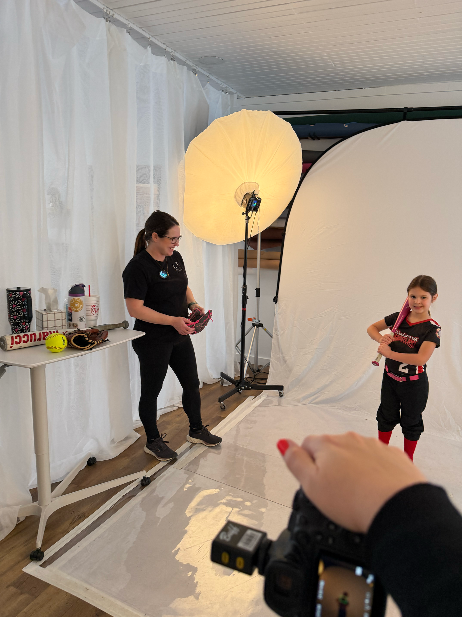 A photographer captures a young child in sports uniform posing in a professional photo studio with umbrella lighting.