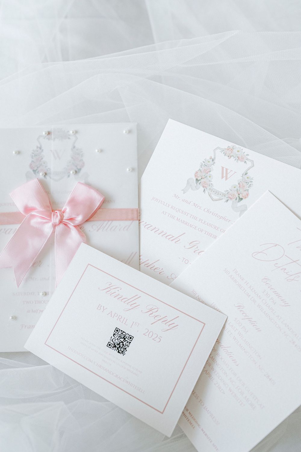 Elegant pink and white wedding invitation suite with satin bow and floral monogram crest design.