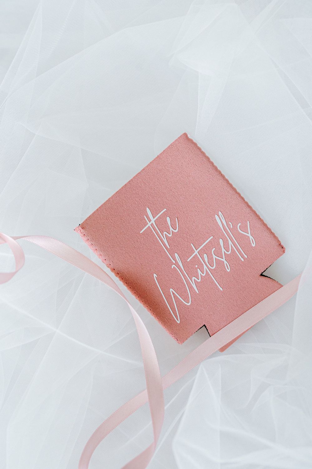 Pink personalized wedding koozie reading The Whitesells on white tulle fabric.