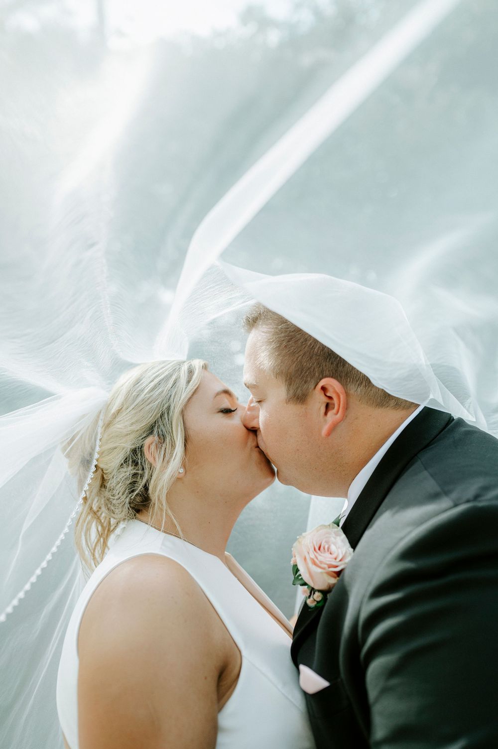 Bride and groom share a romantic kiss under a flowing white veil on their wedding day.