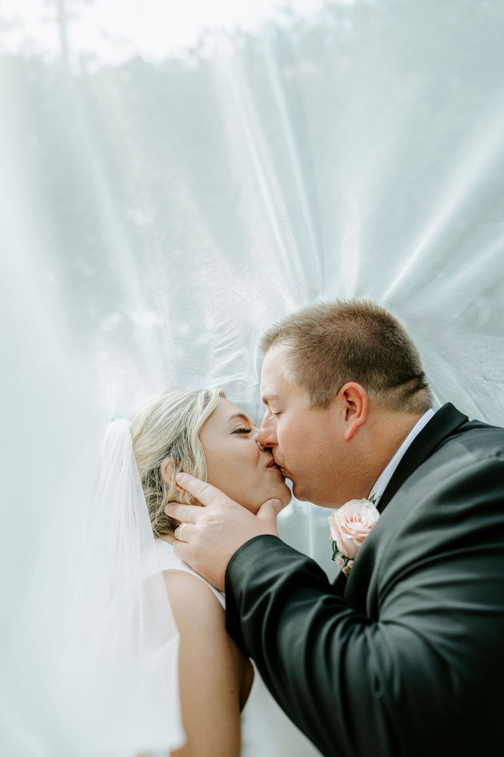 Bride and groom share a tender kiss beneath a flowing white veil on their wedding day.