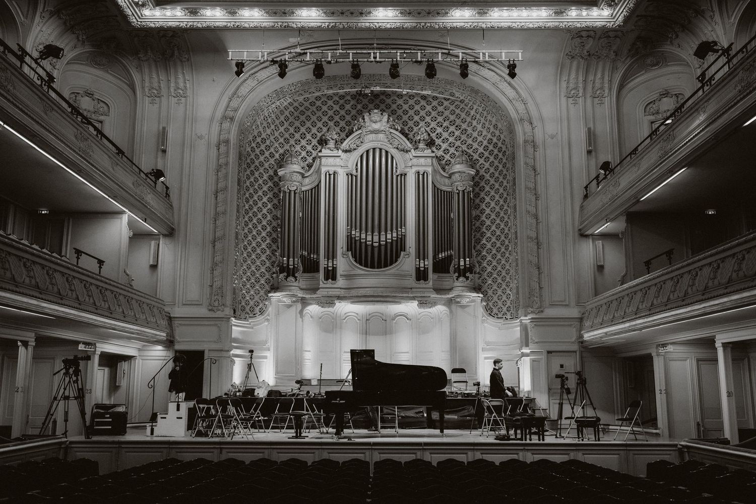Black and white photo of a grand concert hall with a pipe organ, grand piano on stage, and ornate balconies.
