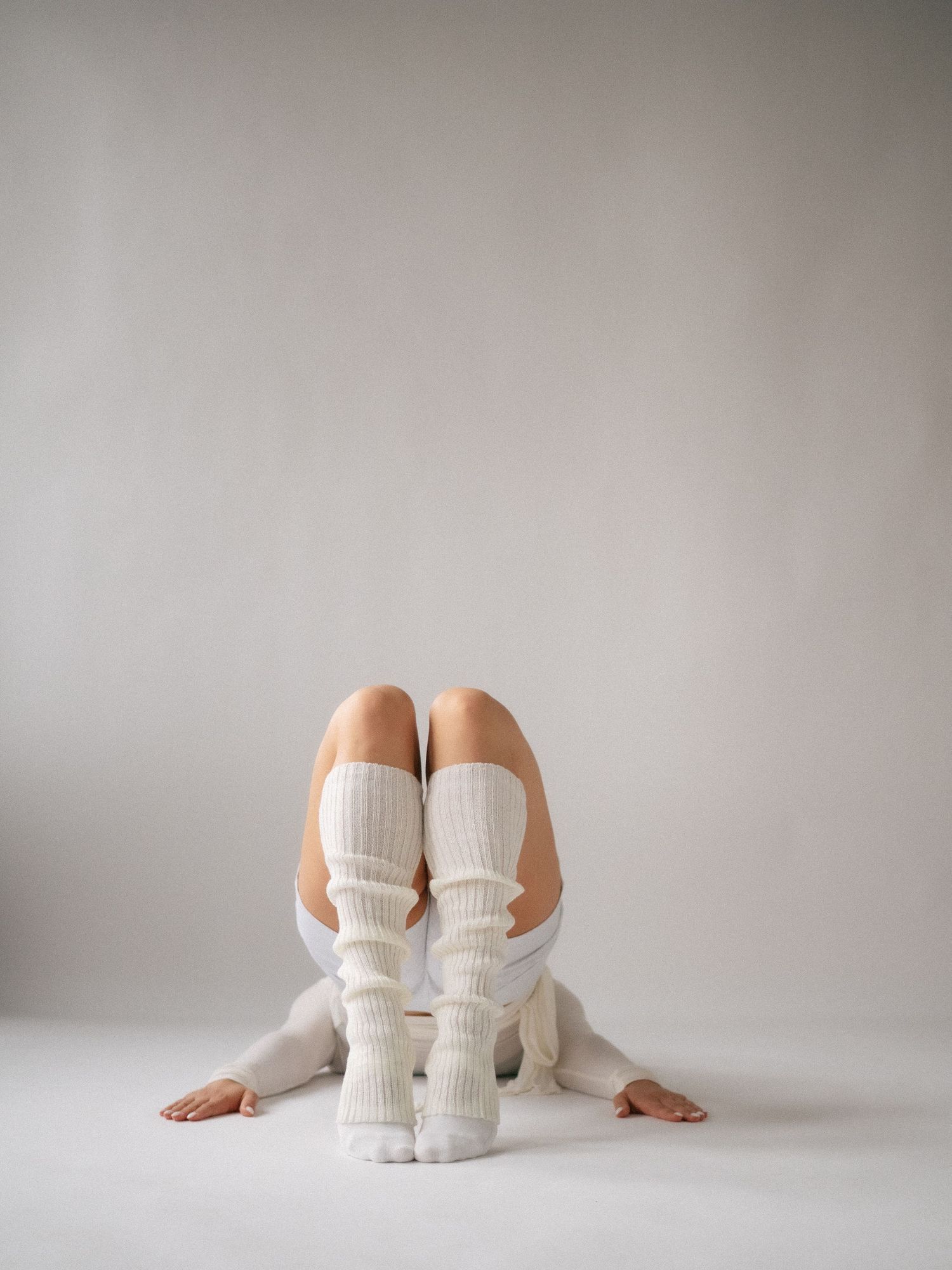 Person sitting on floor wearing white knee-high socks and white shorts against a neutral gray background.