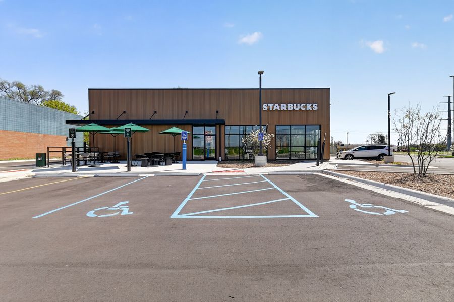 Modern Starbucks coffee shop exterior with accessible parking spaces and outdoor seating area in a fresh strip mall.