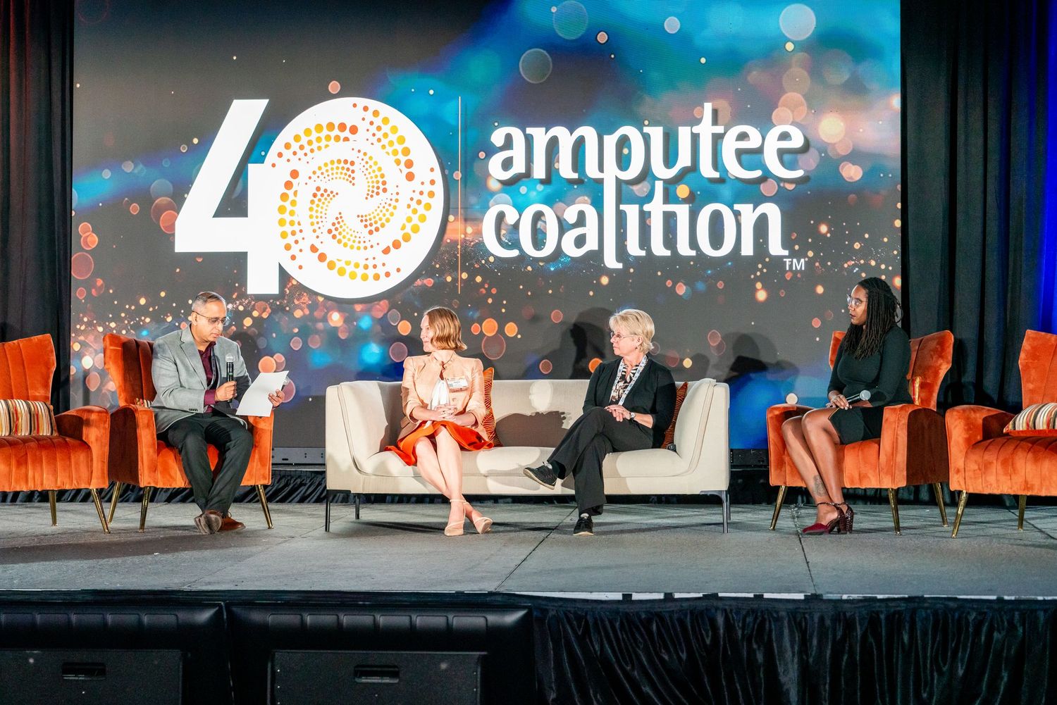 Four panelists seated on stage at the Amputee Coalition 40th anniversary event under a decorative backdrop.