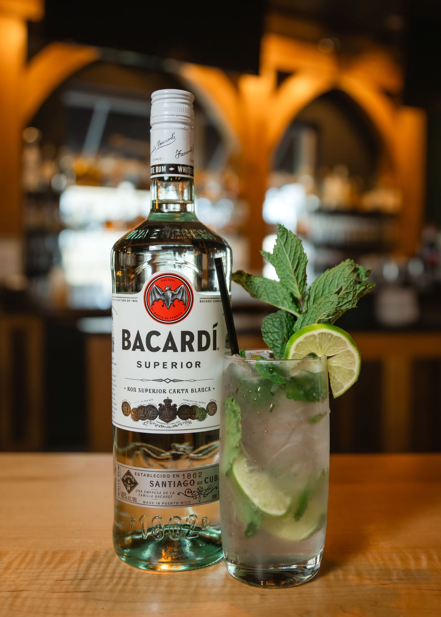 Bacardi Superior rum bottle beside a fresh mojito cocktail with mint and lime on a wooden bar.
