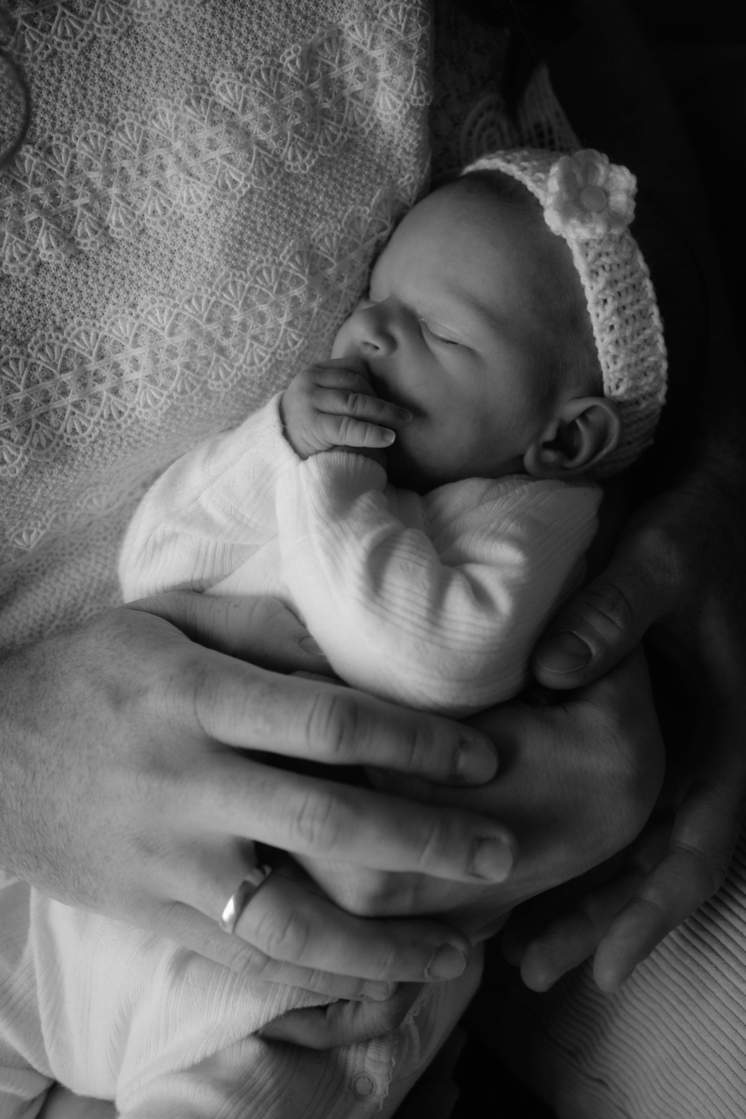 Black and white photo of a sleeping newborn baby in a white knit bonnet cradled in adult hands.