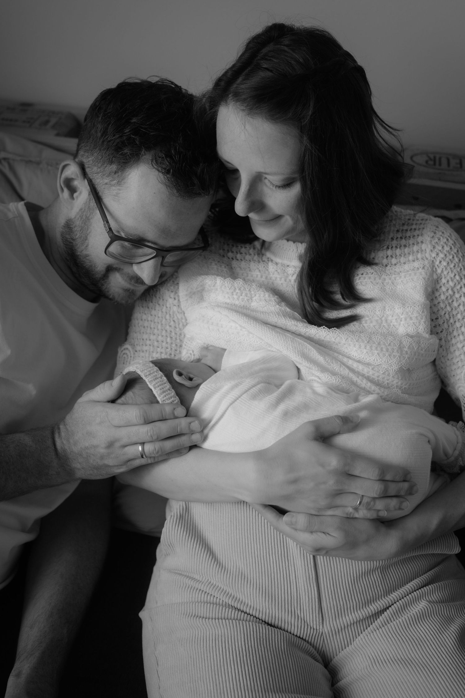 Black and white photo of new parents lovingly gazing at their newborn baby in a hospital room.