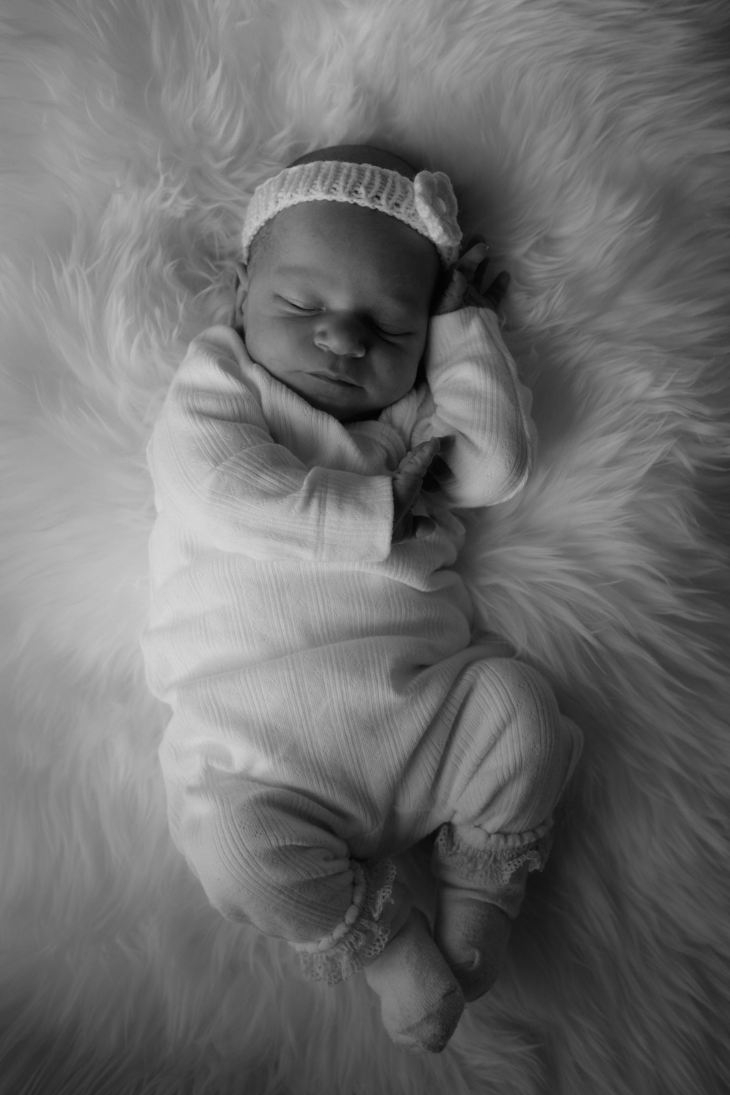 Black and white photo of a sleeping newborn baby wrapped in white clothing on a fluffy blanket.