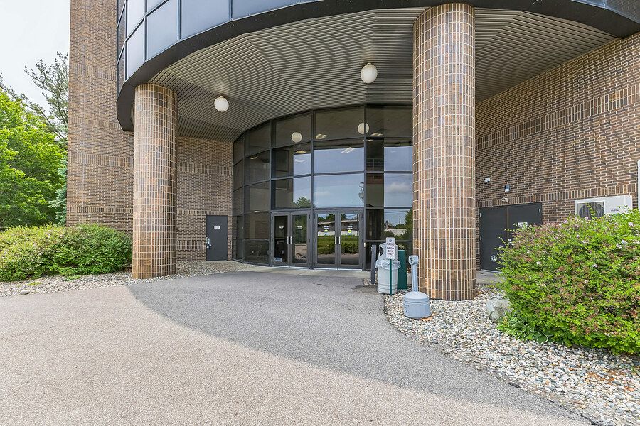 Modern brick office building entrance with curved glass doors, cylindrical columns, and landscaped surroundings.