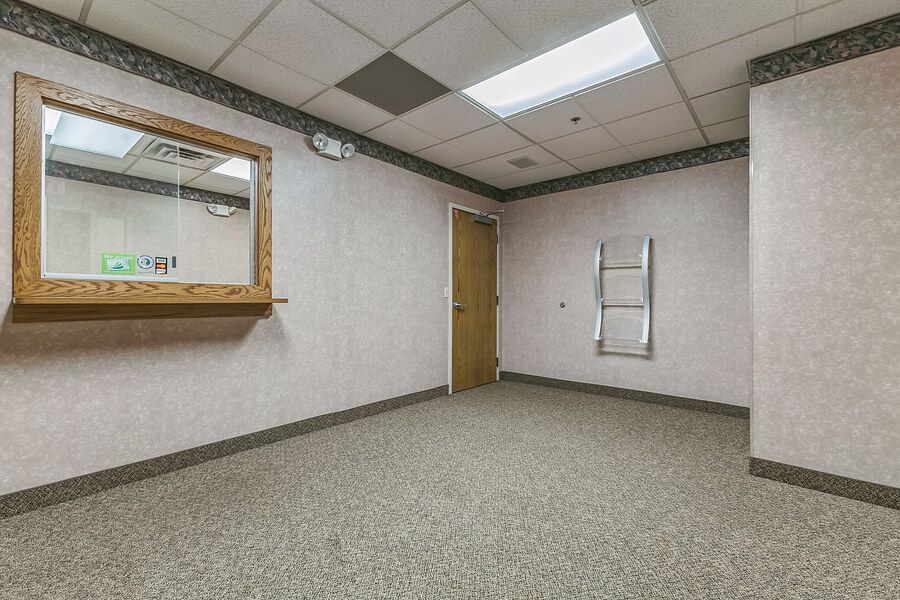 Empty office room with gray carpet, wallpaper, a framed mirror, and a wooden door in a commercial building.