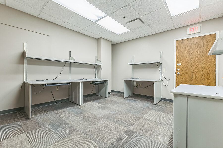 Bright laboratory workspace with built-in countertops, overhead cabinets, and neutral carpet flooring.