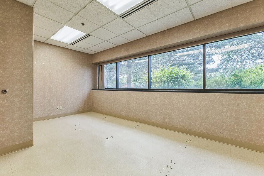 Empty office space with large windows, drop ceiling, and textured walls offering natural light.