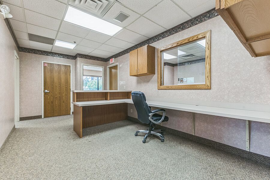 Professional office space with L-shaped desk, black chair, wood cabinets, and large mirror on beige walls.
