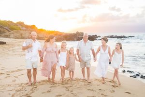 Multi-generational family walking hand-in-hand on a Hawaiian beach at golden hour.