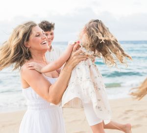 Mother joyfully spinning her daughter on a sunny Hawaiian beach.
