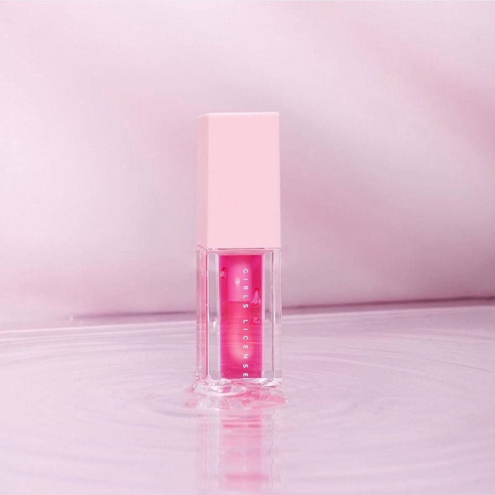 Pink lip gloss tube with vibrant fuchsia formula on a soft pink reflective surface.