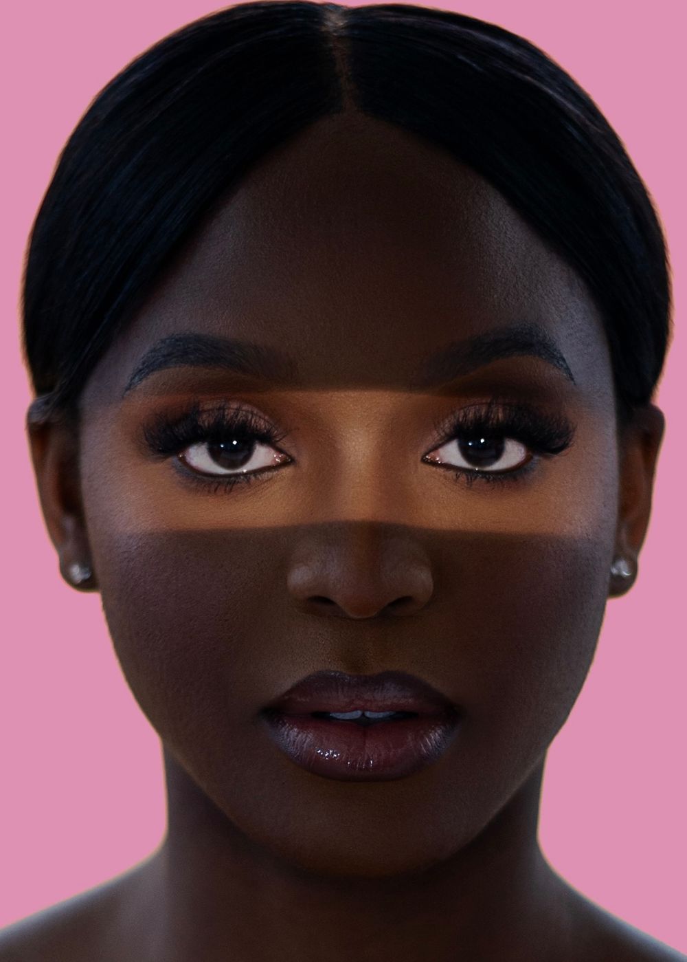 Close-up portrait of a woman with dark skin, smoky eye makeup, and glossy lips on a pink background.