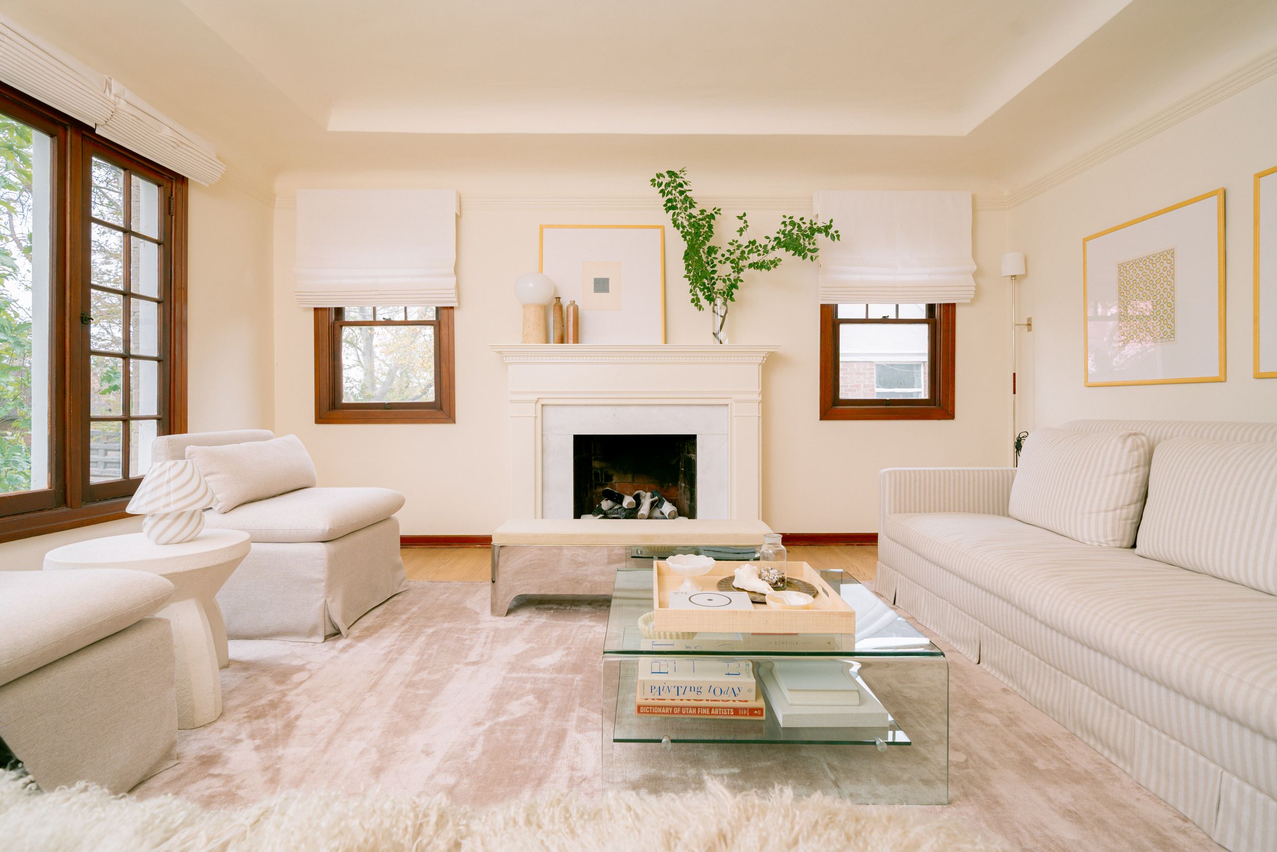 Bright living room with white sofas, glass coffee table, shag rug, and a white fireplace flanked by two windows.
