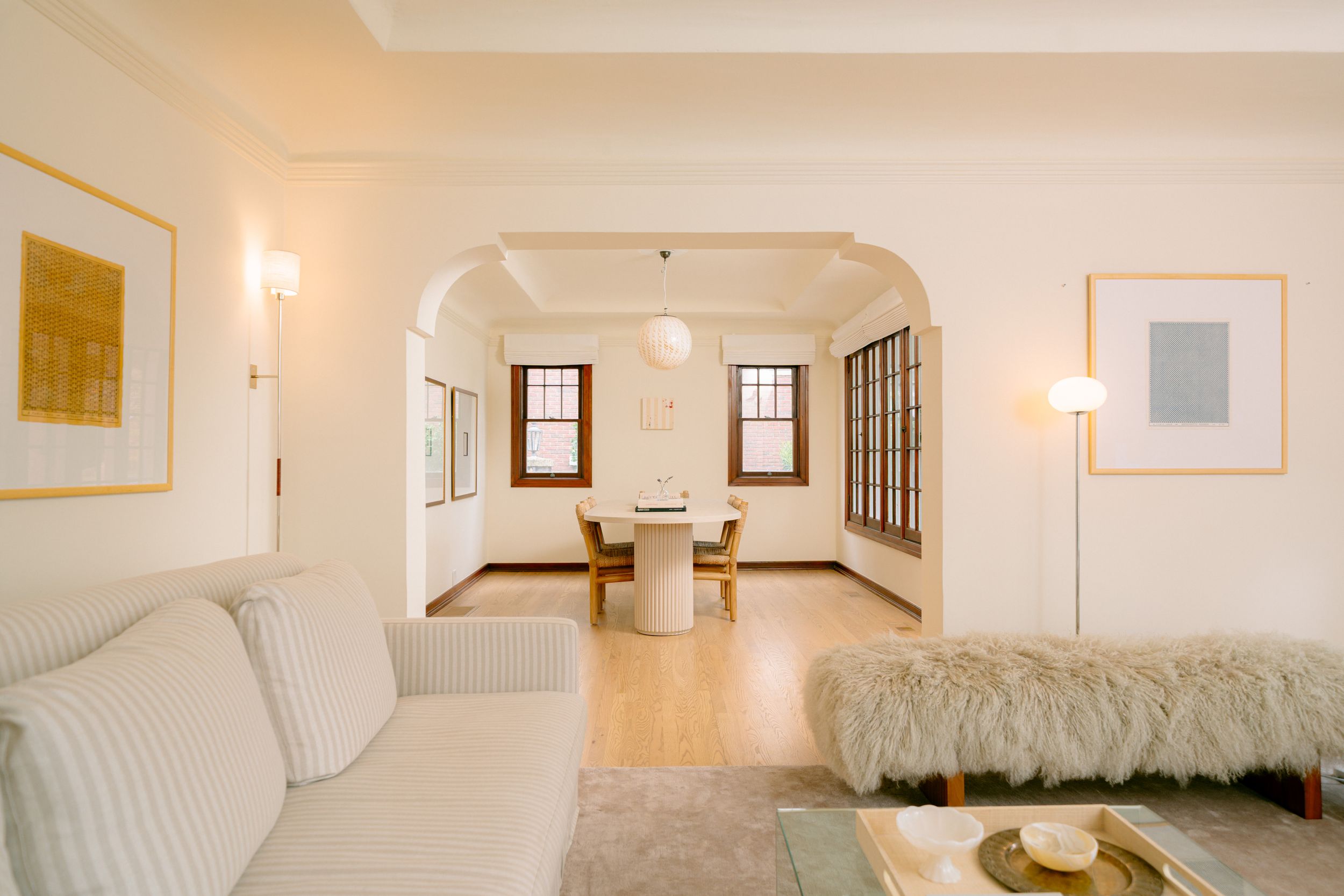 Bright white living room with arched doorway leading to dining area, hardwood floors, and elegant minimalist decor.