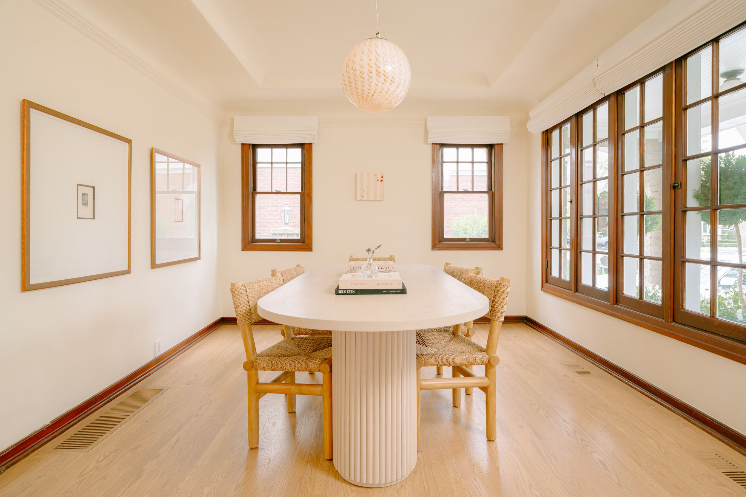 Bright dining room with oval white table, wooden chairs, globe pendant light, hardwood floors, and large windows.