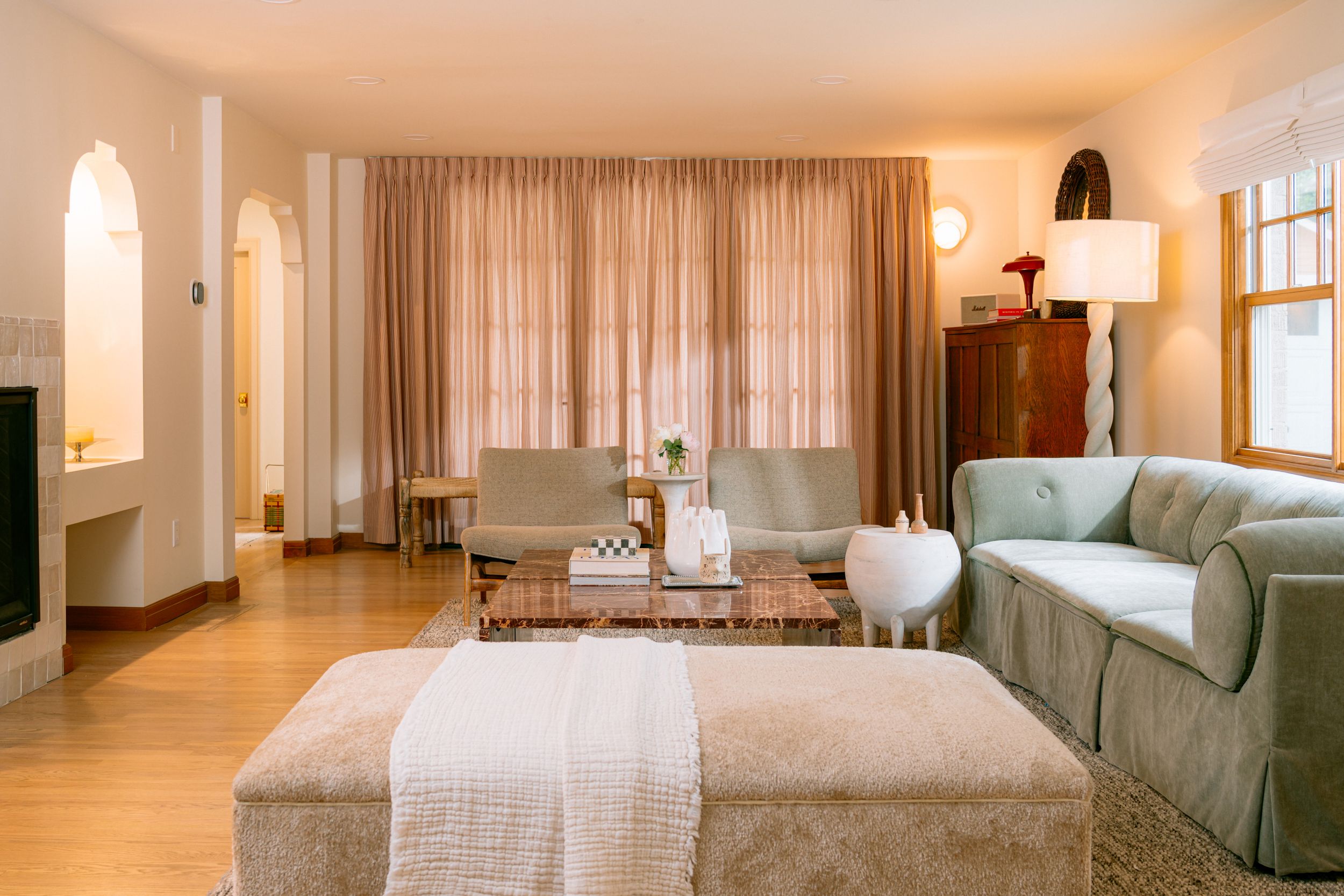 Elegant living room with neutral tones, arched doorways, plush sofa, velvet ottoman, and warm ambient lighting.