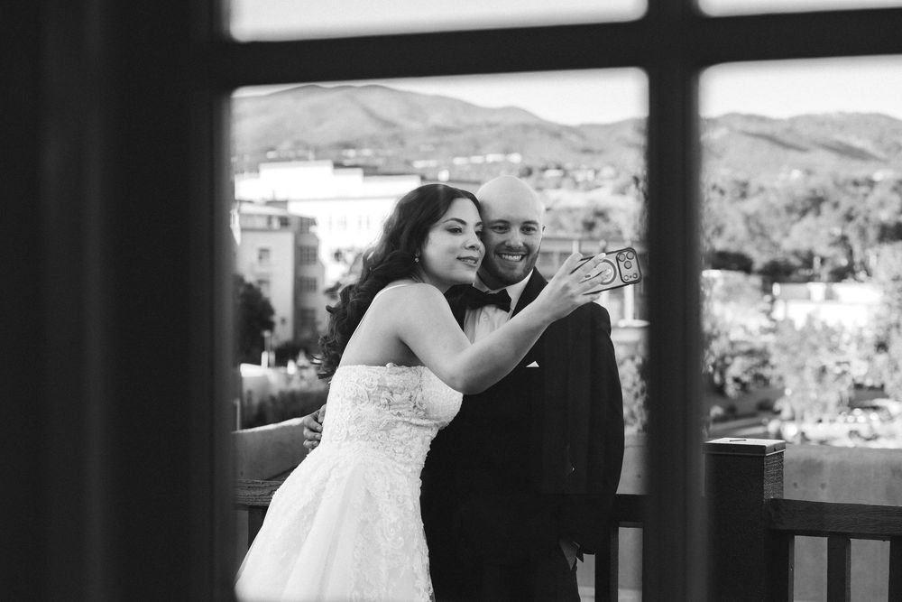 Black and white photo of bride and groom embracing on balcony with mountain views behind them.