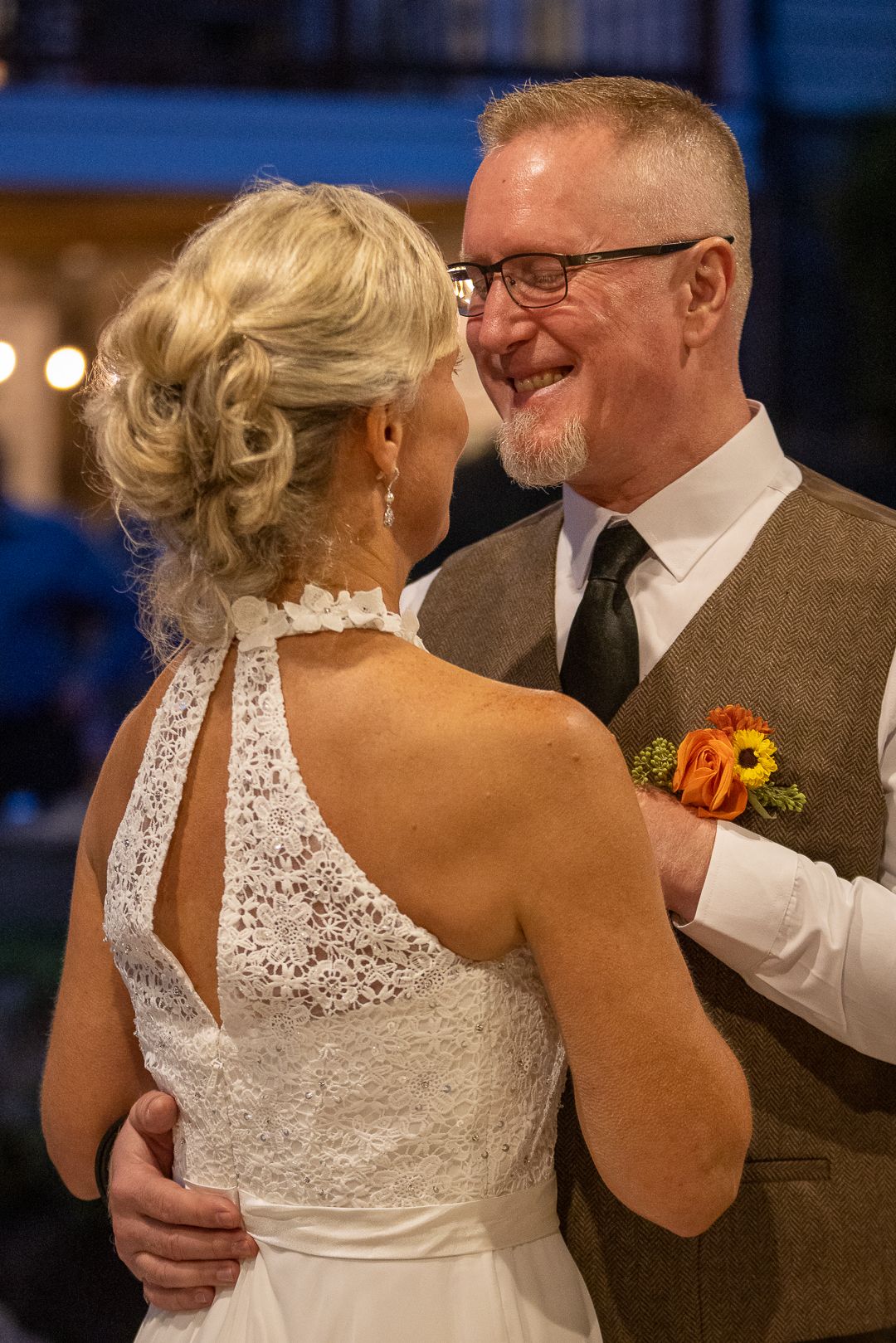 Bride and groom share first dance, woman in lace halter wedding gown, man in brown tweed vest with sunflower boutonniere.
