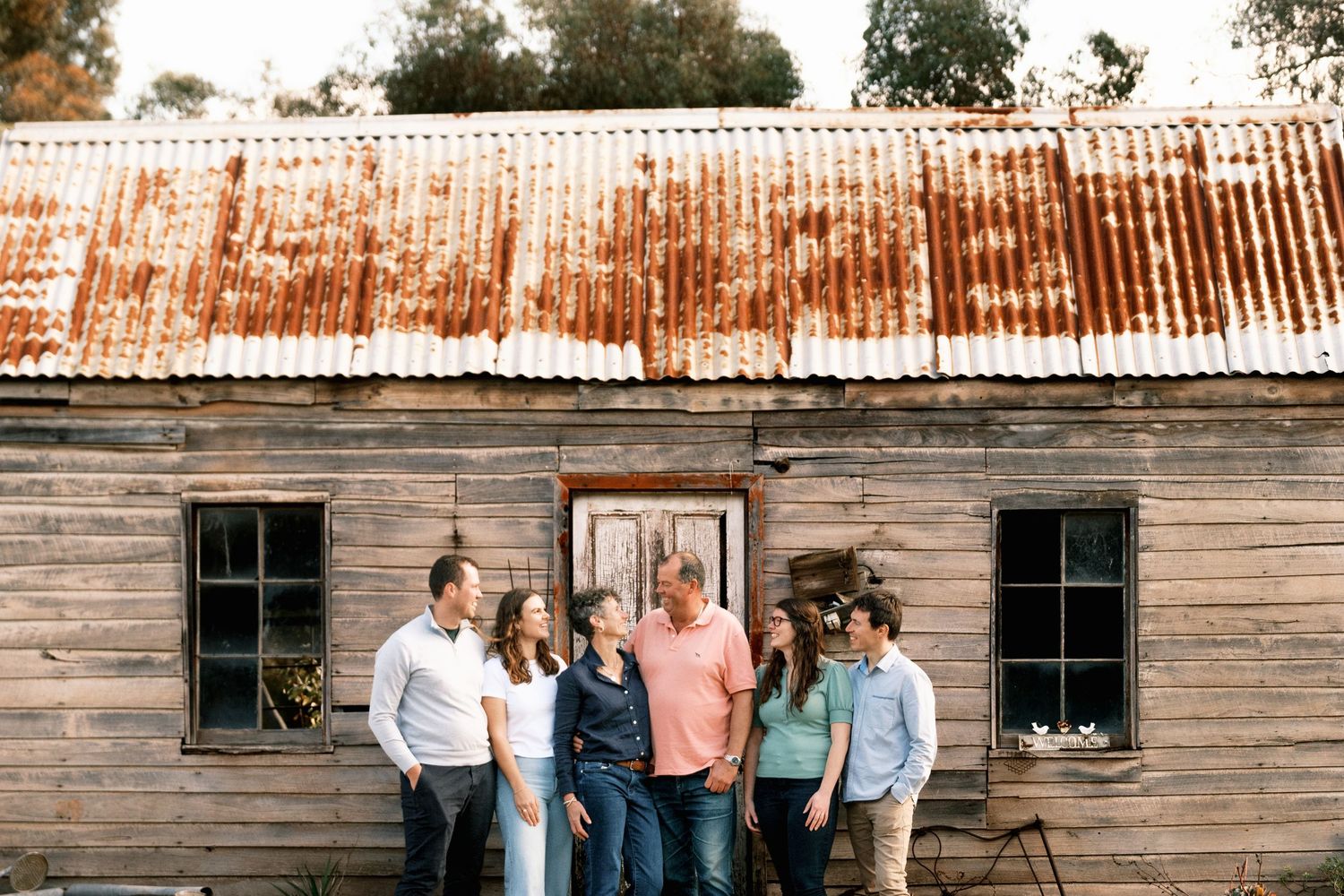 Family of five posing together outside a rustic wooden building with a corrugated iron roof.