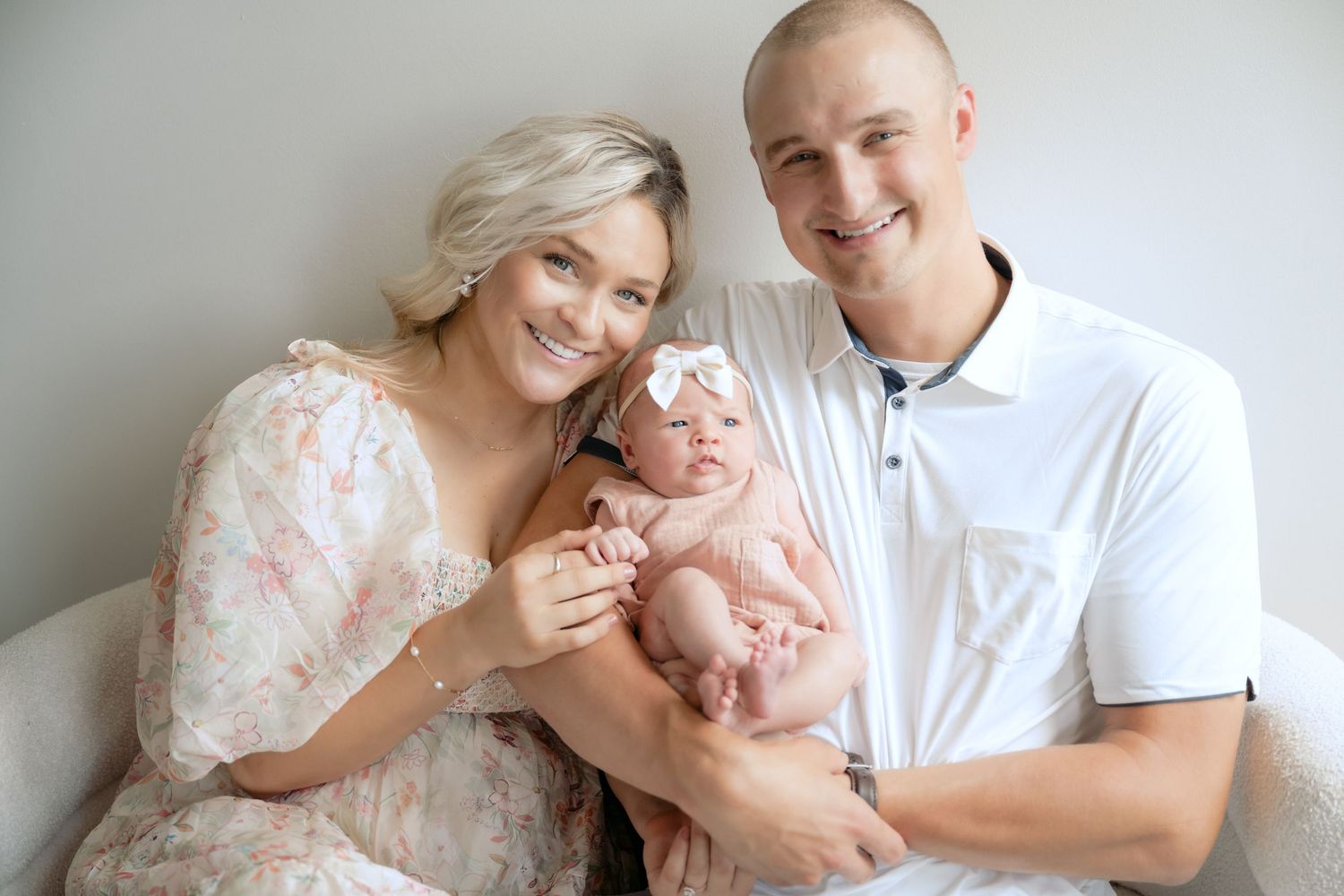 parents seated on a couch smiling at the camera while holding their baby during in-studio lifestyle newborn session in stillwater, mn