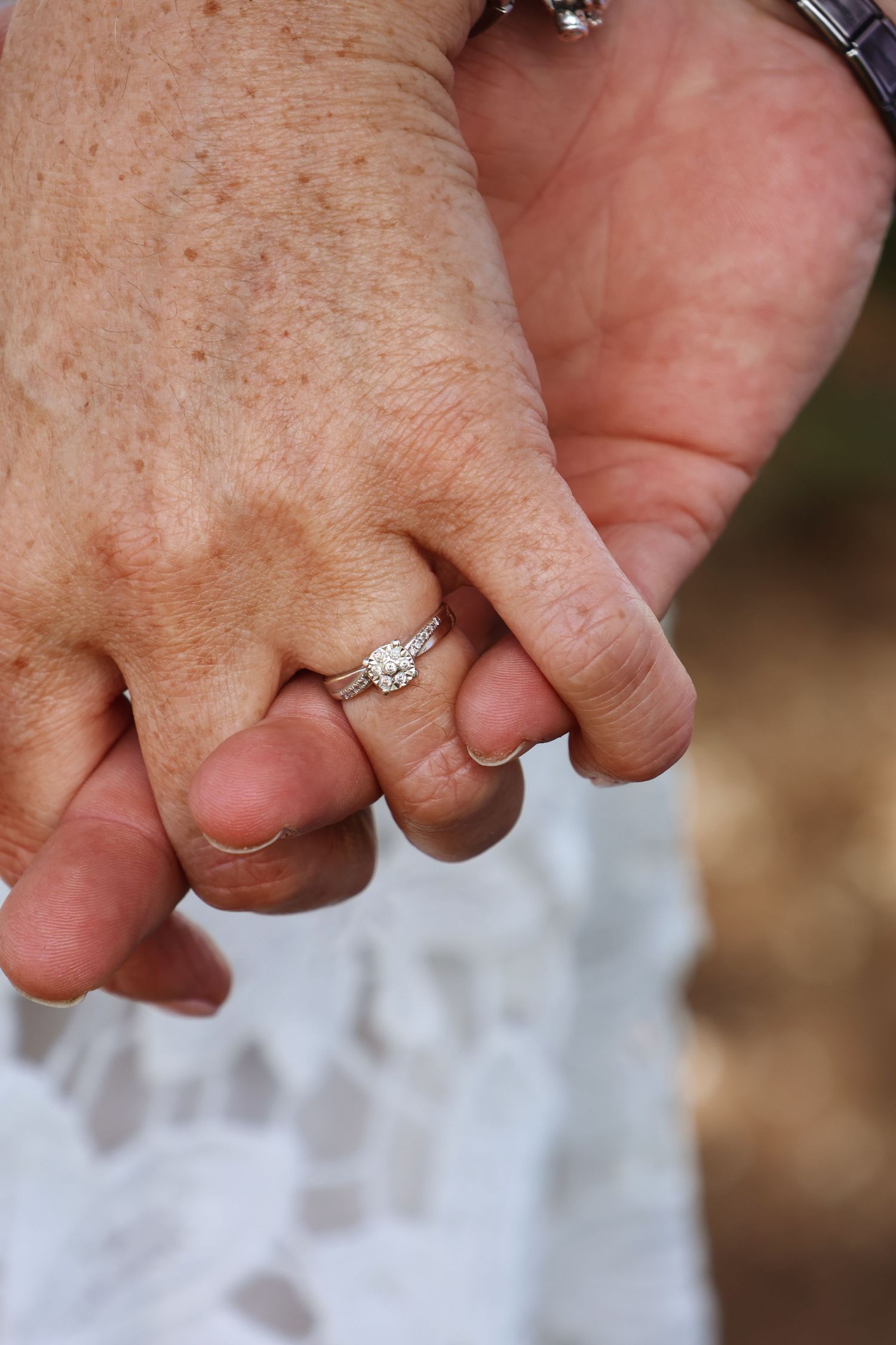 Close-up of two hands holding, woman wearing a diamond engagement ring, symbolizing love and commitment.