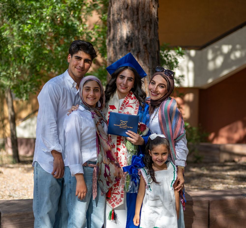 Graduate in blue cap and gown celebrates with family of five outdoors at graduation ceremony.