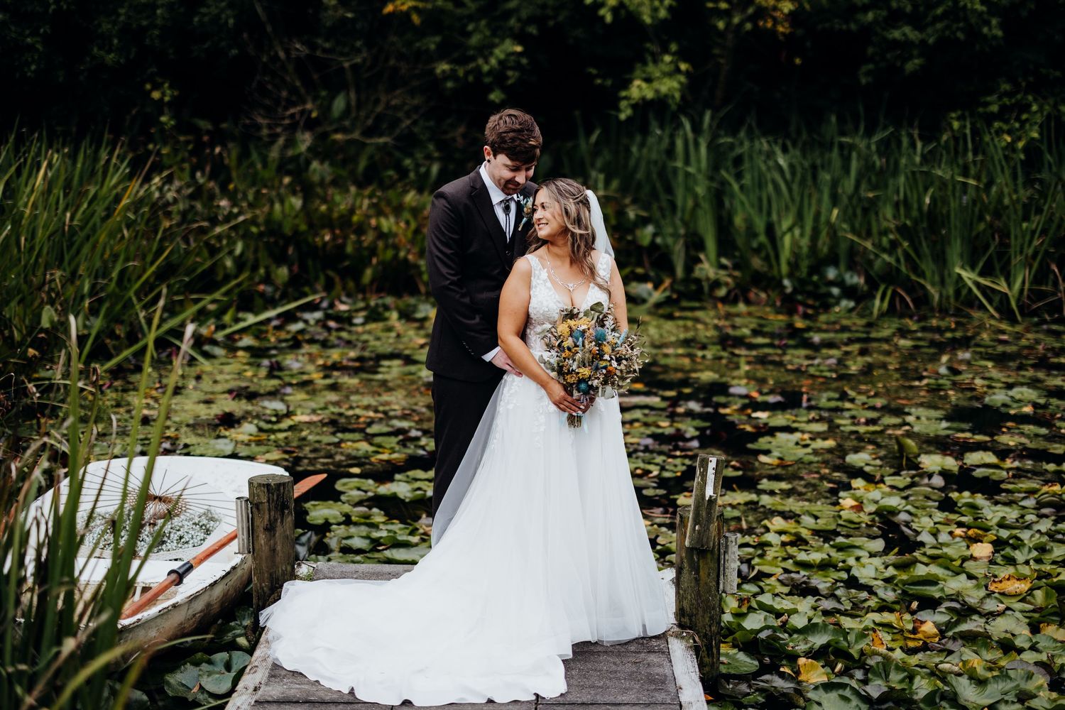 A couple shares a romantic moment on a dock overlooking a serene lake surrounded by trees.
