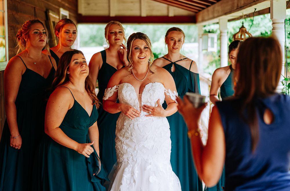 Bride in white lace gown smiles with bridesmaids in teal dresses during wedding preparations.