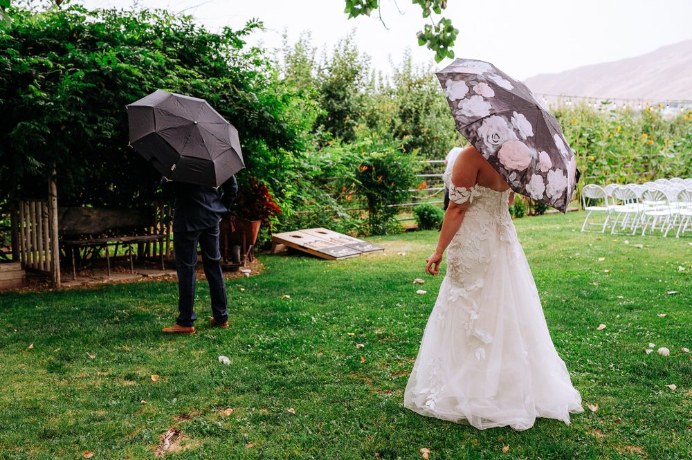 Bride and groom share a romantic first look moment in a garden, each holding an umbrella on a rainy wedding day.