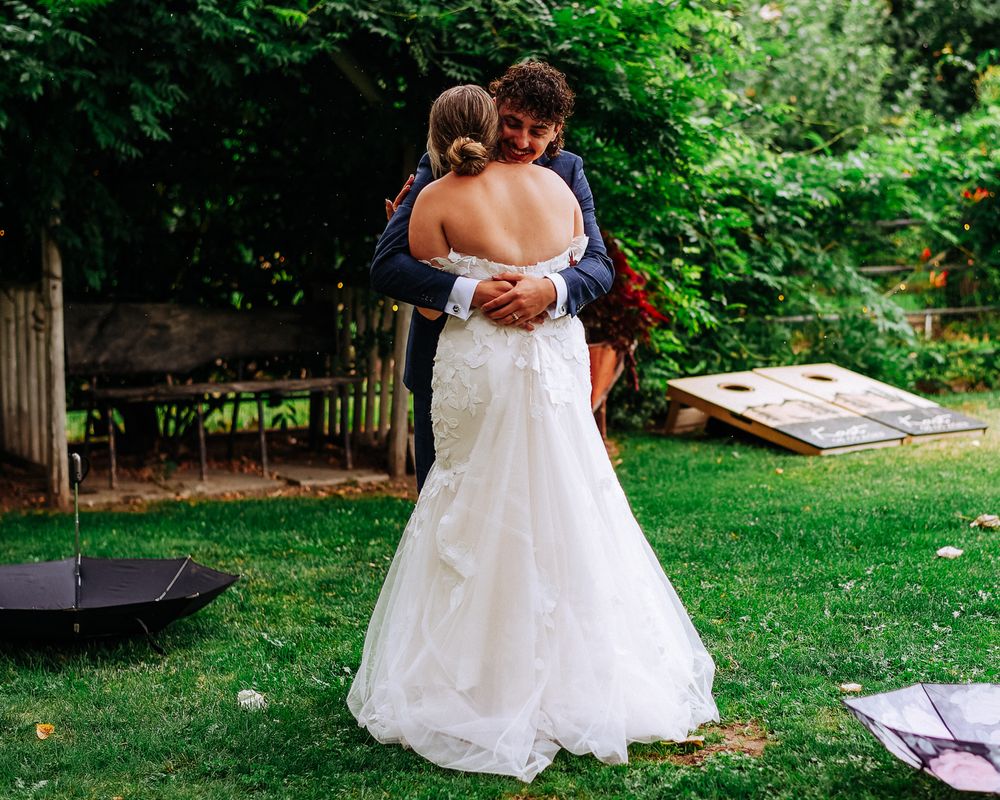 Bride and groom share a tender embrace in a lush garden during their outdoor wedding celebration.